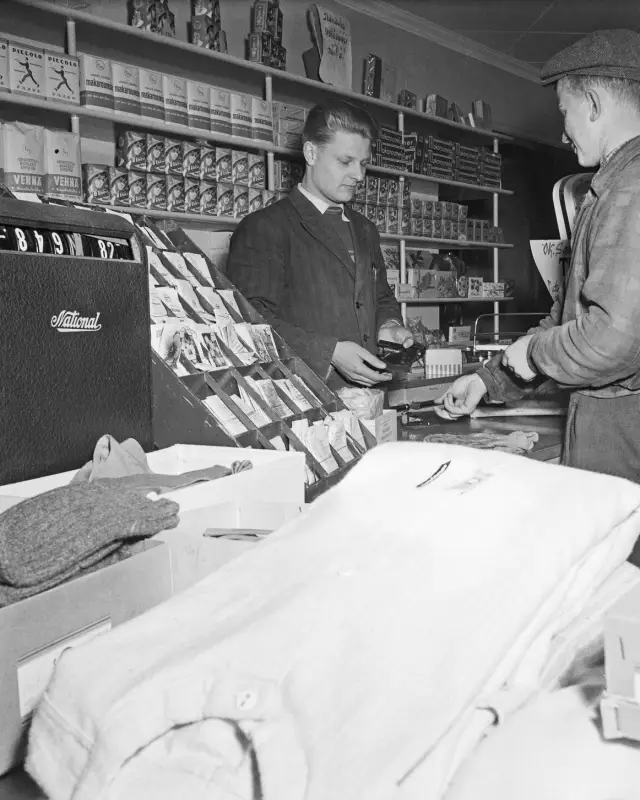 Kauppias tiskin takana kassakoneen vieressä ottaa vastaan asiakkaan maksua.